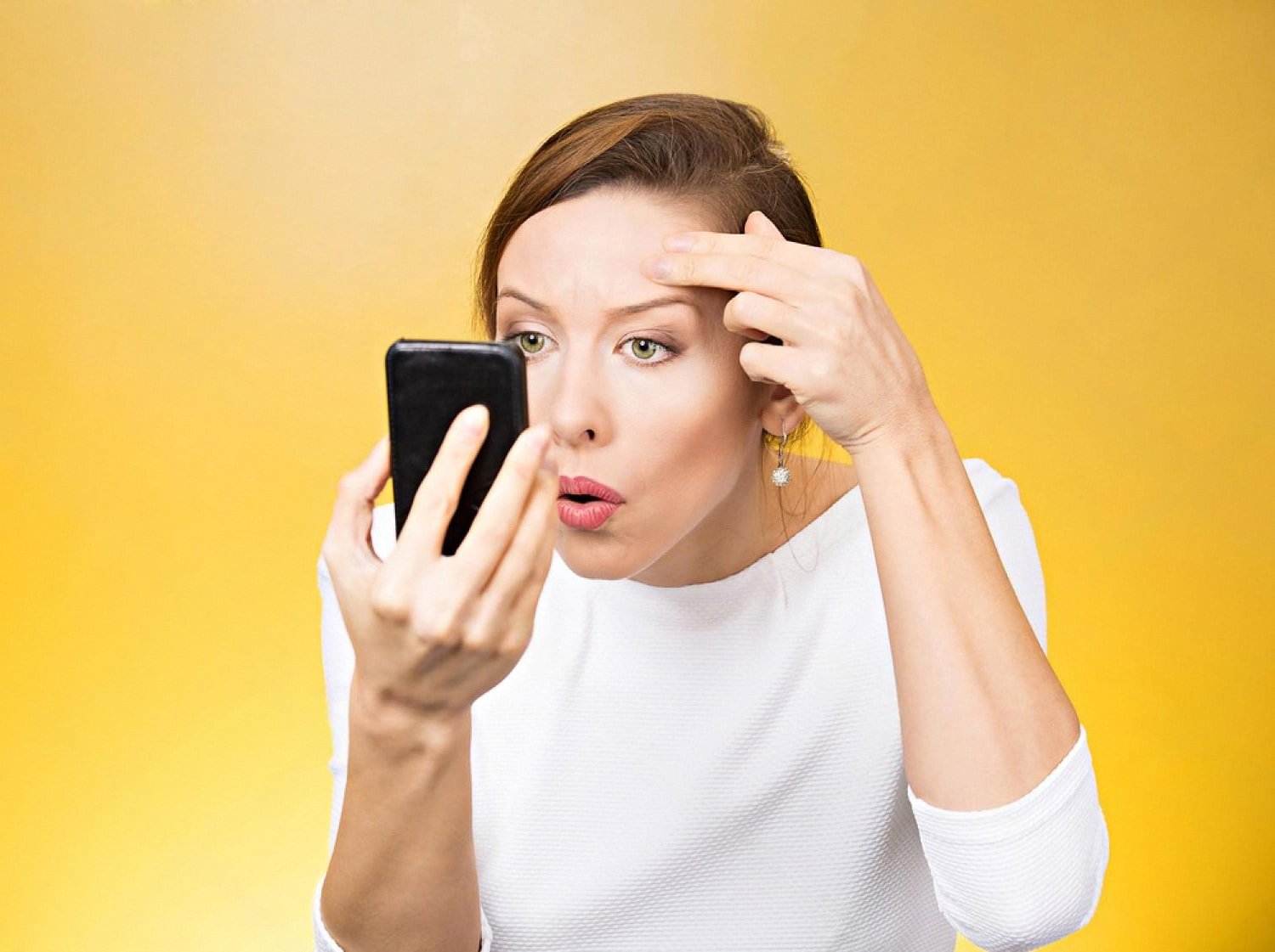 Woman checking her forehead in a phone mirror for post-acne marks and pigmentation