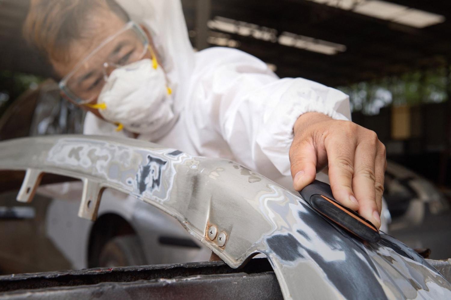 Detailer in protective gear performing paint correction on a car bumper